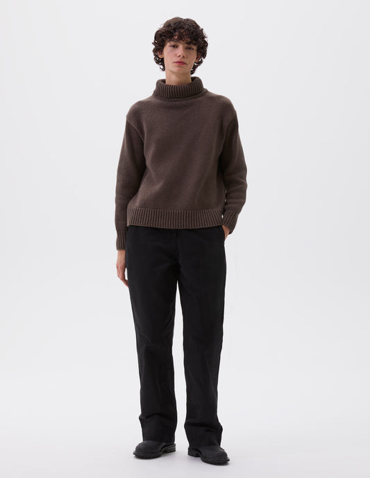 Full body image, front view of model wearing relaxed brown high neck jumper with deep rib trim on neck, cuffs and hem. Styled with black trousers and black leather boots.