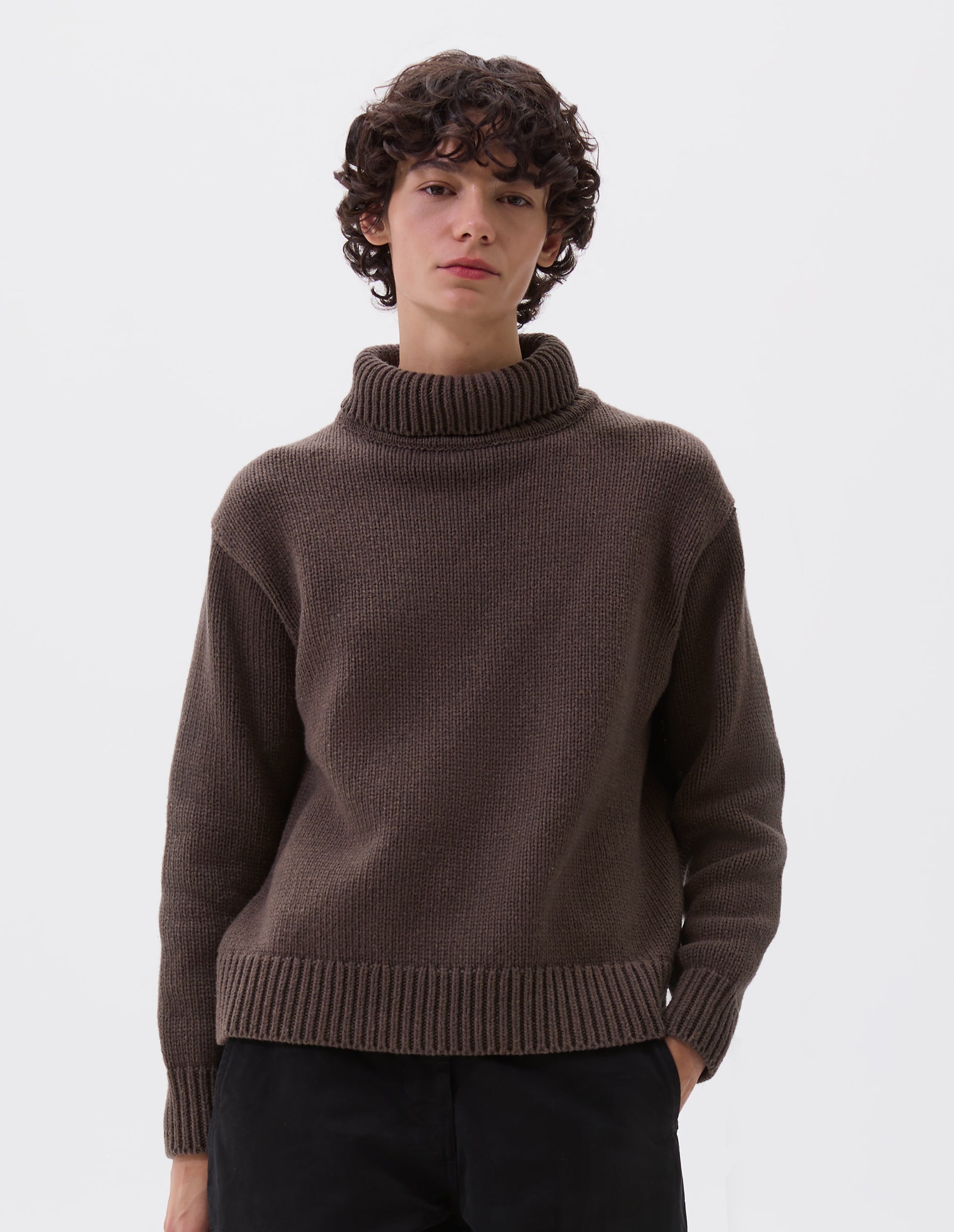 Cropped image, front view of model wearing relaxed brown high neck jumper with deep rib trim on neck, cuffs and hem. Styled with black trousers.