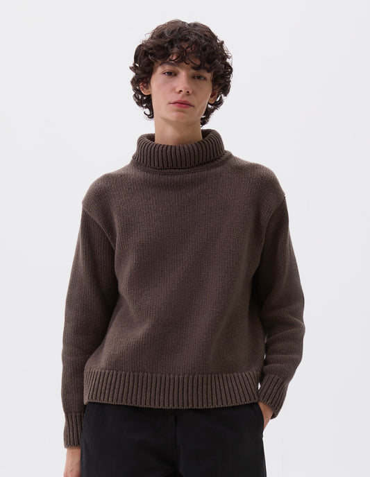 Cropped image, front view of model wearing relaxed brown high neck jumper with deep rib trim on neck, cuffs and hem. Styled with black trousers.