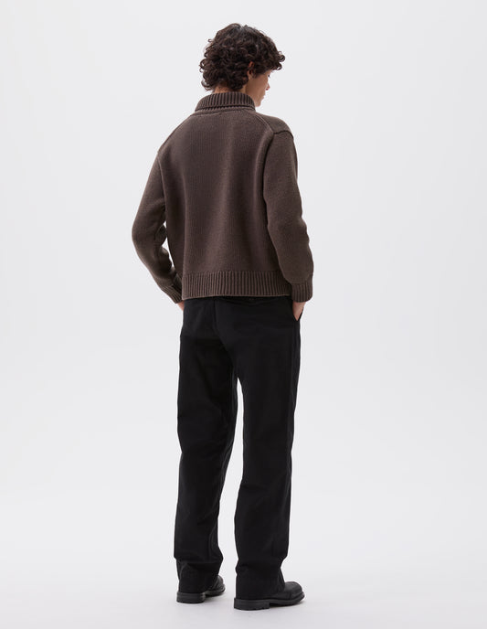 Full body image, back view of model wearing relaxed brown high neck jumper with deep rib trim on neck, cuffs and hem. Styled with black trousers and black leather boots.