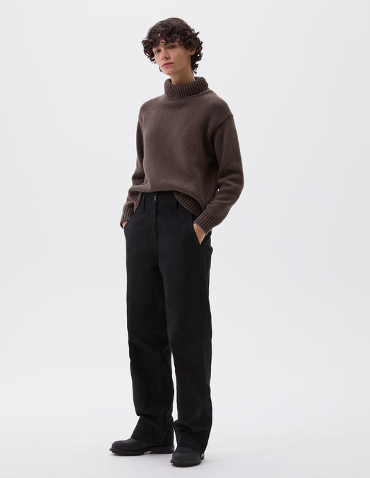 Full body image, front view of model wearing black cotton canvas trousers with stitch through waistband, button fastening, dropped belt loops and concealed slant pockets. Styled with brown high neck jumper and black leather boots.