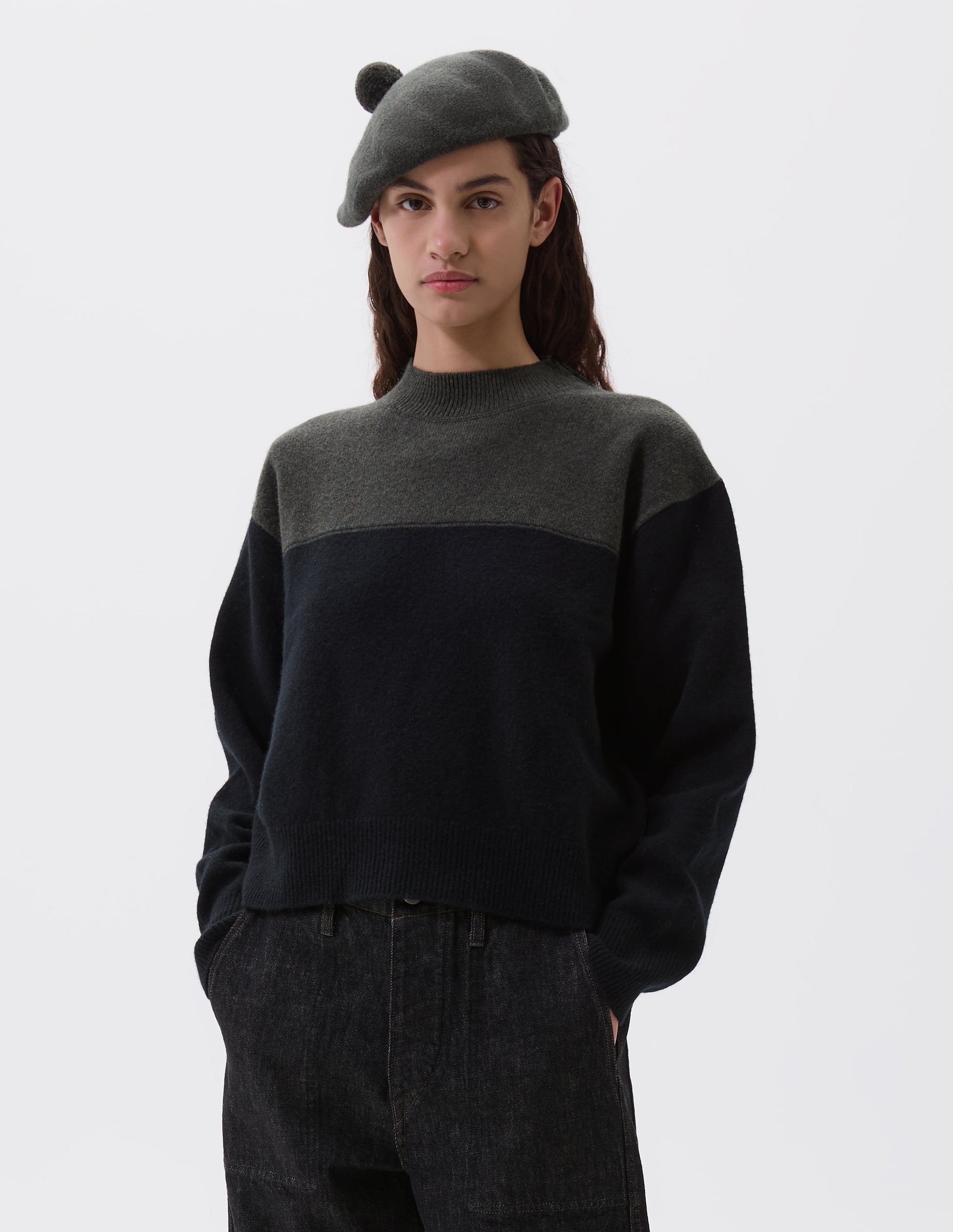 Cropped body image, front view of female model wearing green wool tam o shanter hat with matching pom pom bobble in centre. Styled black and green jumper and black denim jeans.