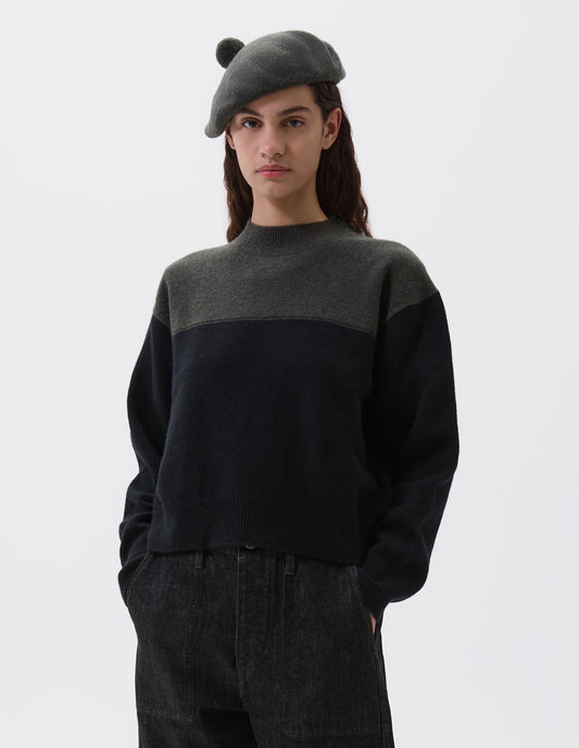 Cropped body image, front view of female model wearing green wool tam o shanter hat with matching pom pom bobble in centre. Styled black and green jumper and black denim jeans.