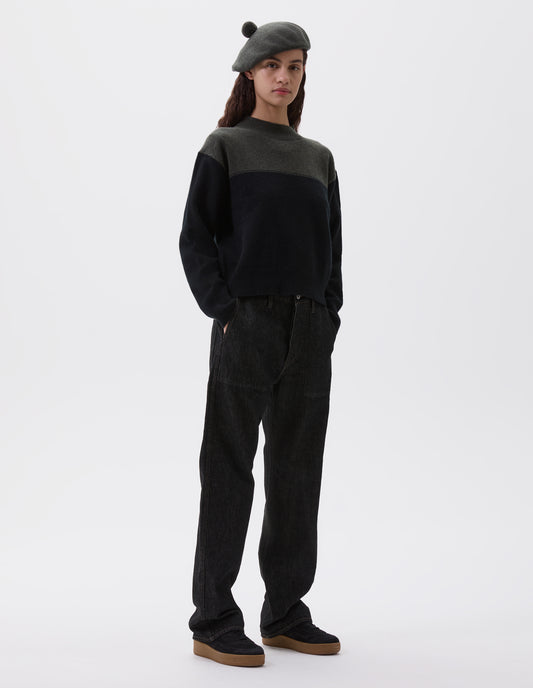 Full body image, front view of model wearing cropped dark green and black jumper with ribbed crew neck, cuffs and hem. Styled with dark green beret and black jeans with black nubuck trainers.