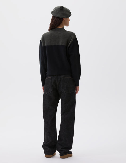 Full body image, back view of model wearing cropped dark green and black jumper with ribbed crew neck, cuffs and hem. Styled with dark green beret and black jeans with black nubuck trainers.