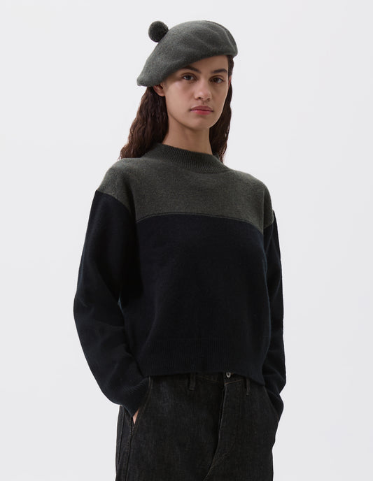 Cropped image, front view of model wearing cropped dark green and black jumper with ribbed crew neck, cuffs and hem. Styled with dark green beret and black jeans.