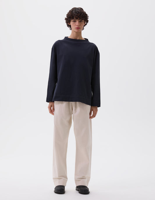 Full body image, front view of model wearing dark blue smock neck long sleeve t-shirt. Styled with white joggers and black leather boots.