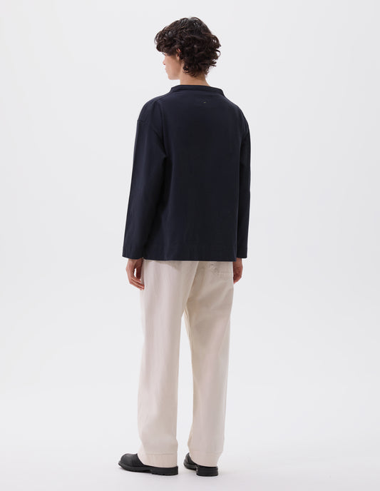 Full body image, back view of model wearing dark blue smock neck long sleeve t-shirt. Styled with white joggers and black leather boots.