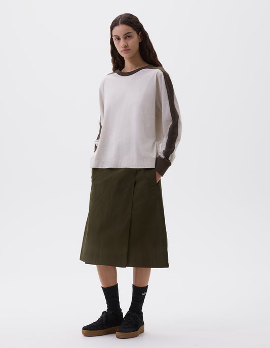 Full body image, front view of model wearing white long sleeve t-shirt with contrasting green stripe on cuffs, arms and neckline. Styled with green skirt with side pockets, black socks and black nubuck trainers.
