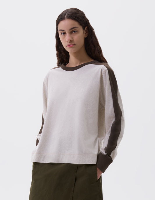 Cropped image, front view of model wearing white long sleeve t-shirt with contrasting brown green stripe on cuffs, arms and neckline. Styled with green skirt.