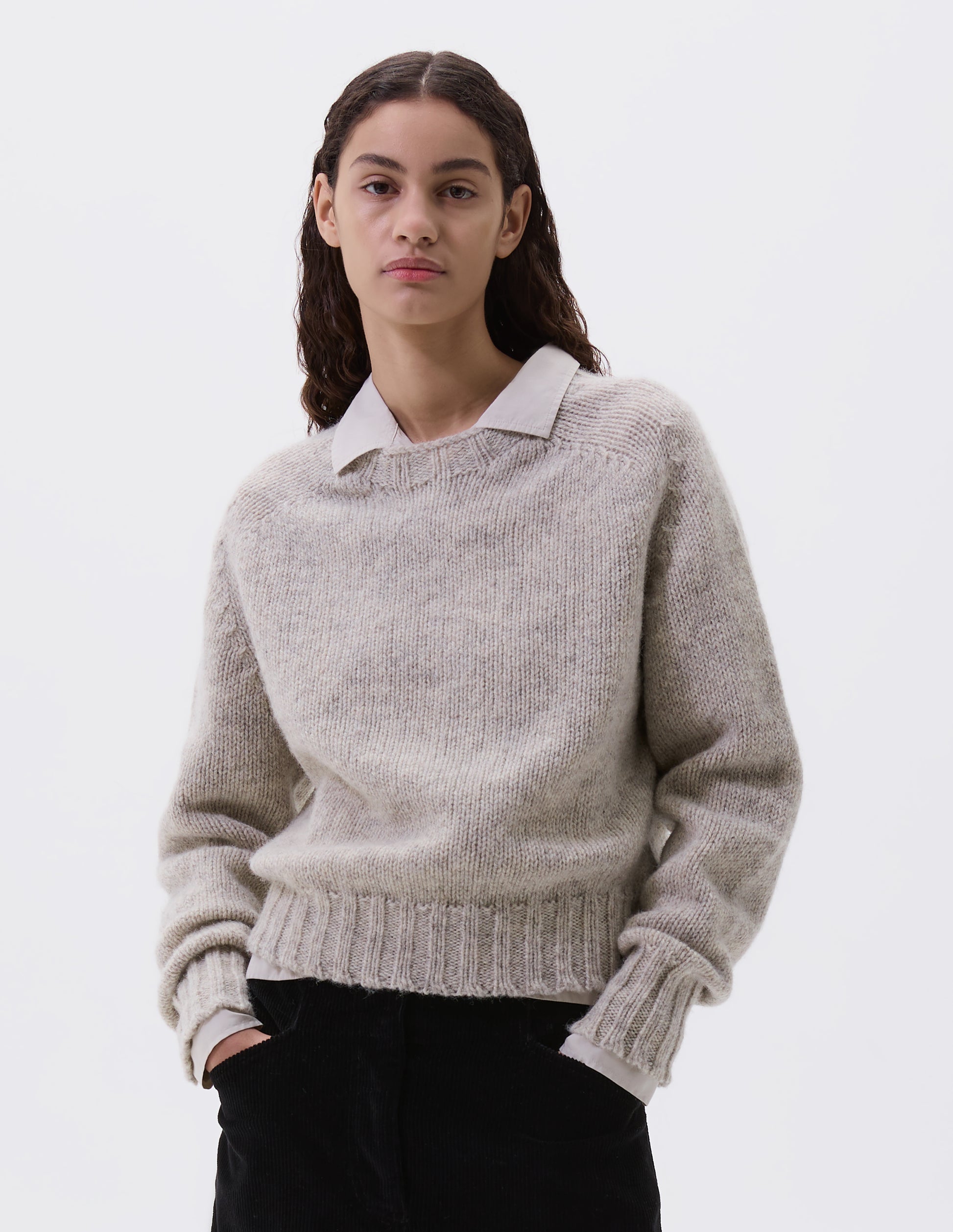 Cropped body image, front view of model wearing beige rustic wool jumper with saddle sleeve and contrasting rib on neck, cuffs and hem. Styled with white shirt and black trousers.