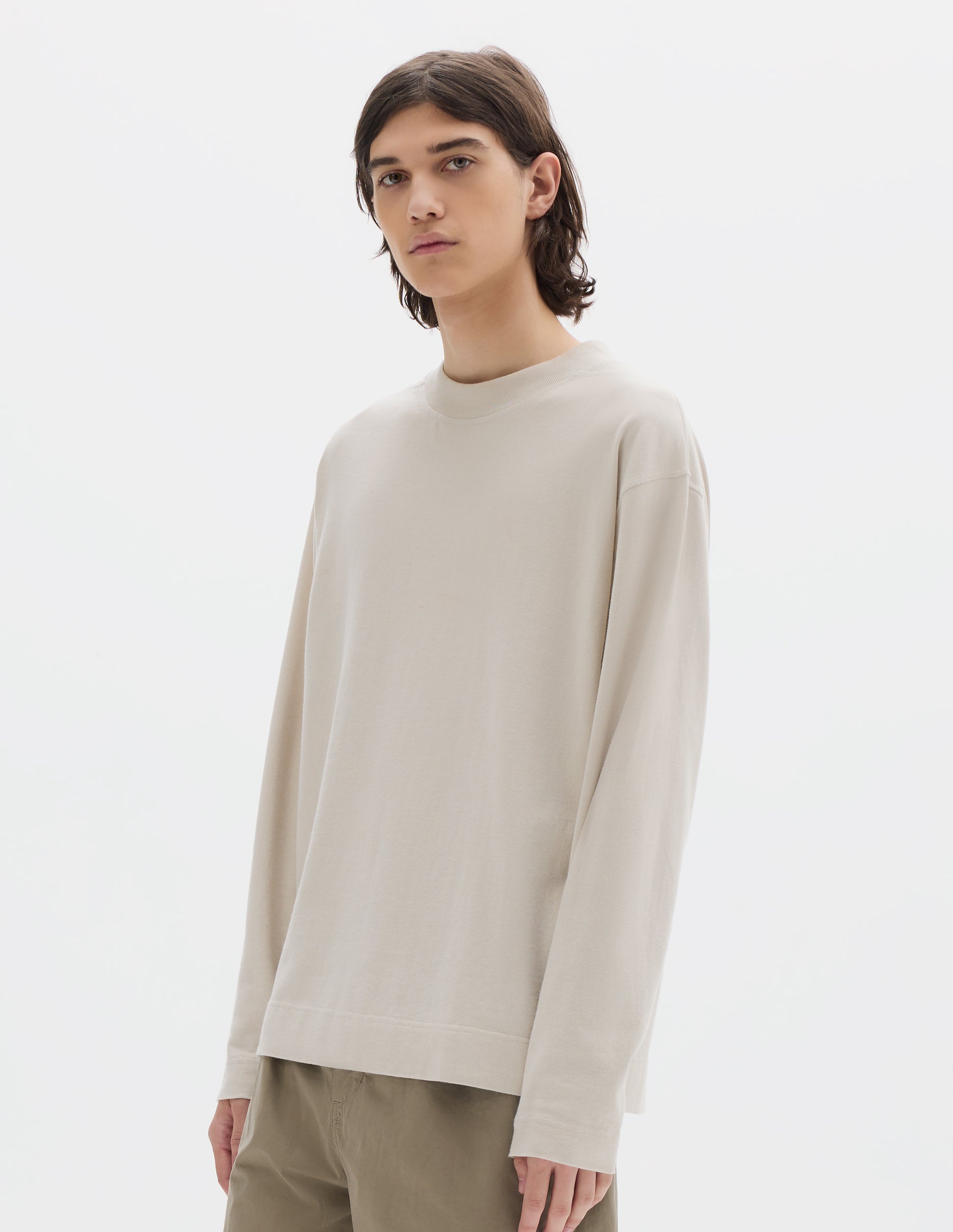 Cropped body image, front view of model wearing an off white long sleeve, flatlock stitching, a deep ribbed collar and ribbed triangle insert on the shoulder. Styled with faded khaki green trousers.