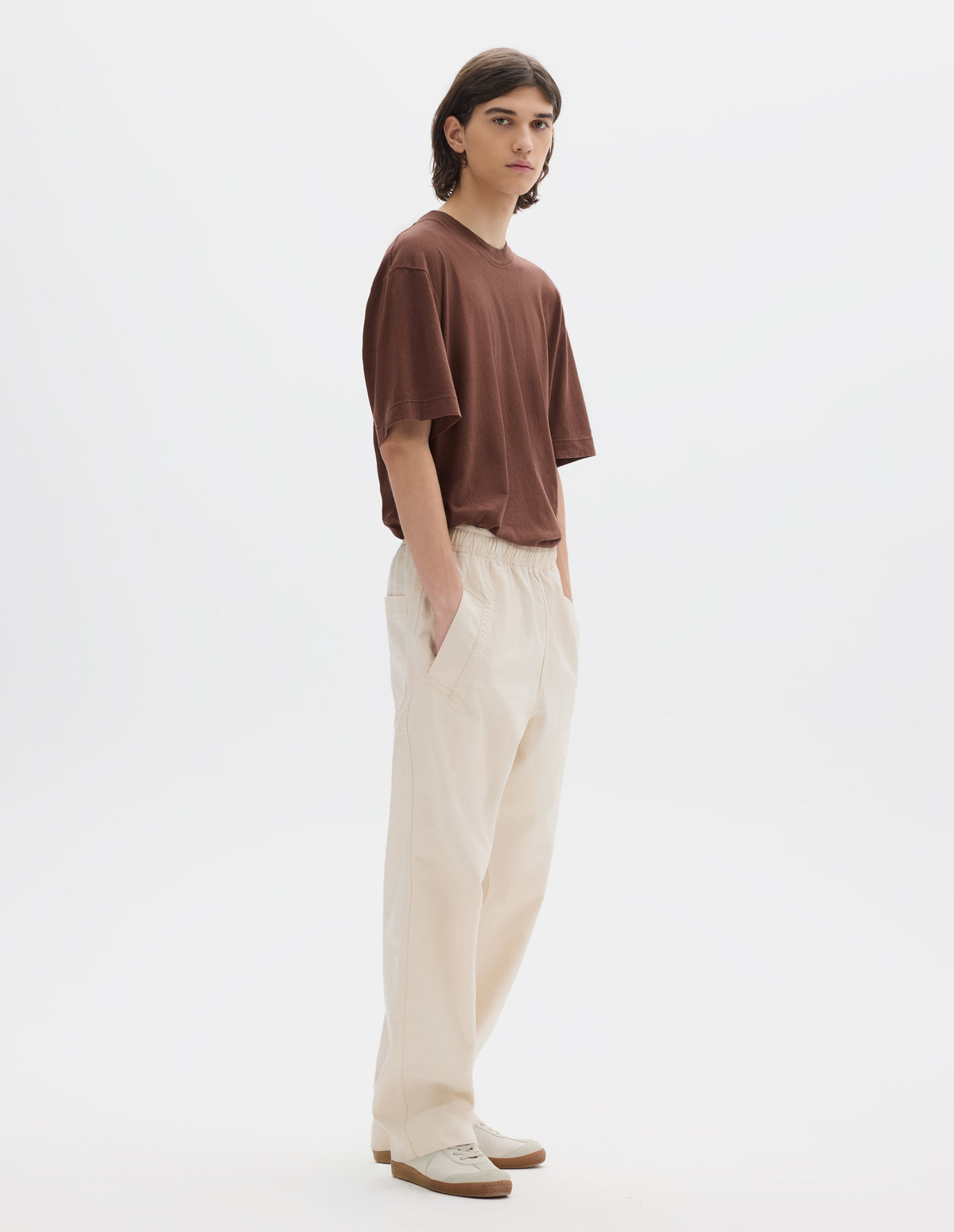 Full body image, front view of model wearing relaxed white joggers with elasticated waist and deep welt pockets. Styled with a brown t-shirt and white suede trainers.