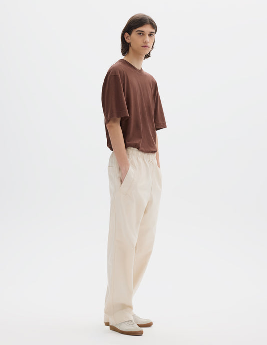 Full body image, front view of model wearing relaxed white joggers with elasticated waist and deep welt pockets. Styled with a brown t-shirt and white suede trainers.