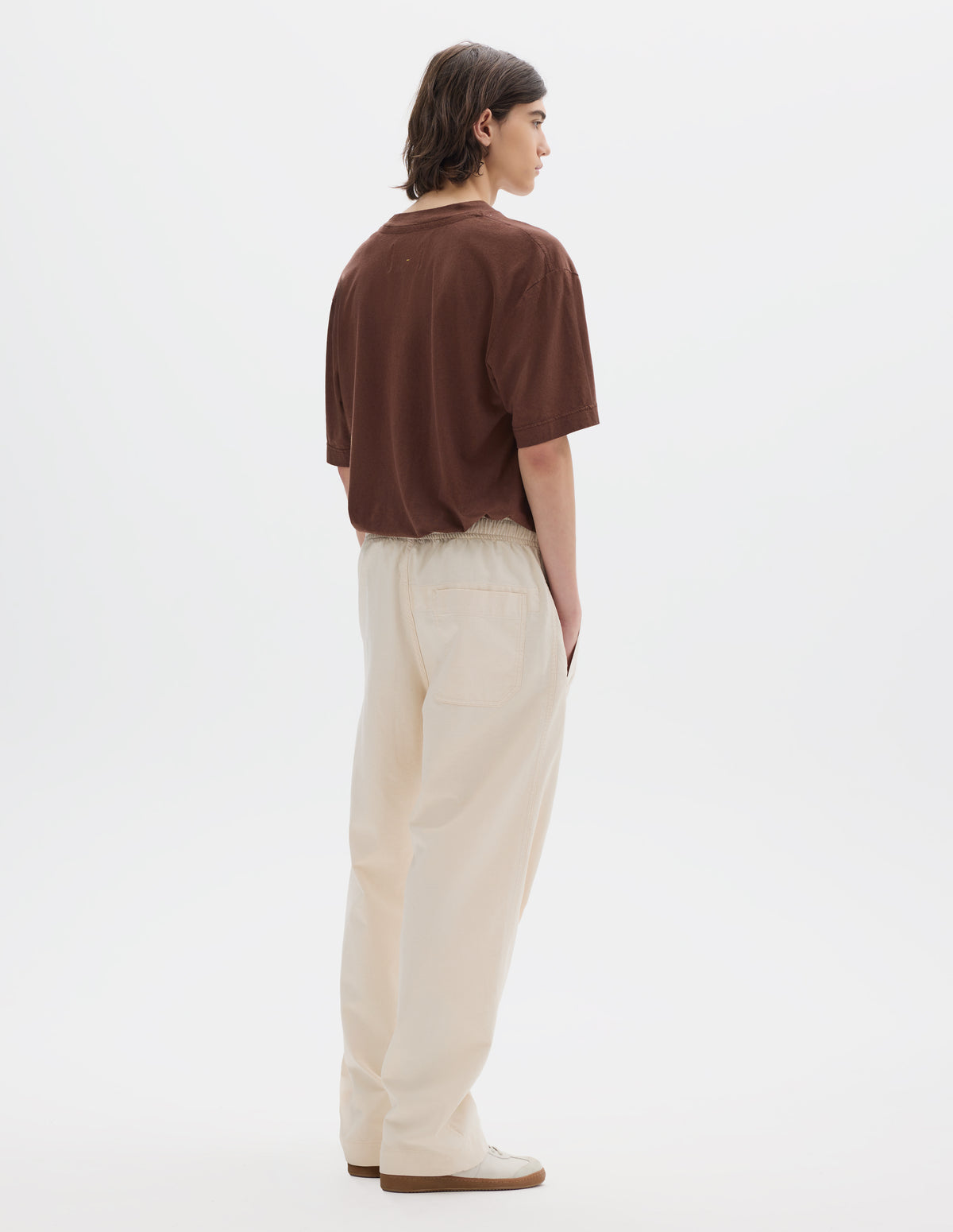 Full body image, back view of model wearing relaxed white joggers with elasticated waist and patch back pocket. Styled with a brown t-shirt and white suede trainers.