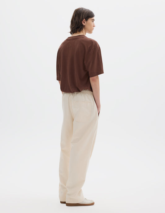 Full body image, back view of model wearing relaxed white joggers with elasticated waist and patch back pocket. Styled with a brown t-shirt and white suede trainers.