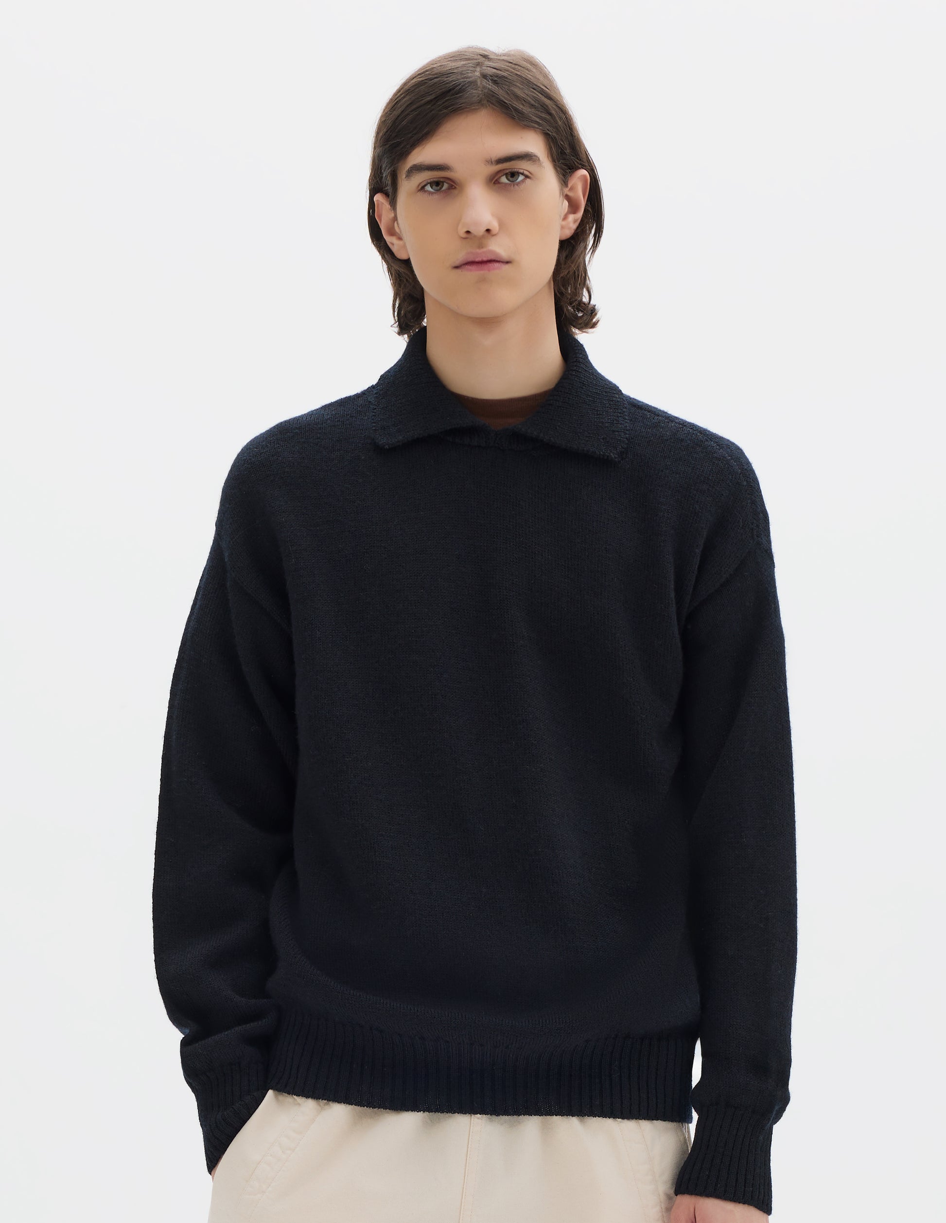 Cropped body image, front view of model wearing a black wool collared sweater  with a wide rib linked on collar, plain knit body, and deeper ribbed cuffs. Styled with off white jogger style trousers.