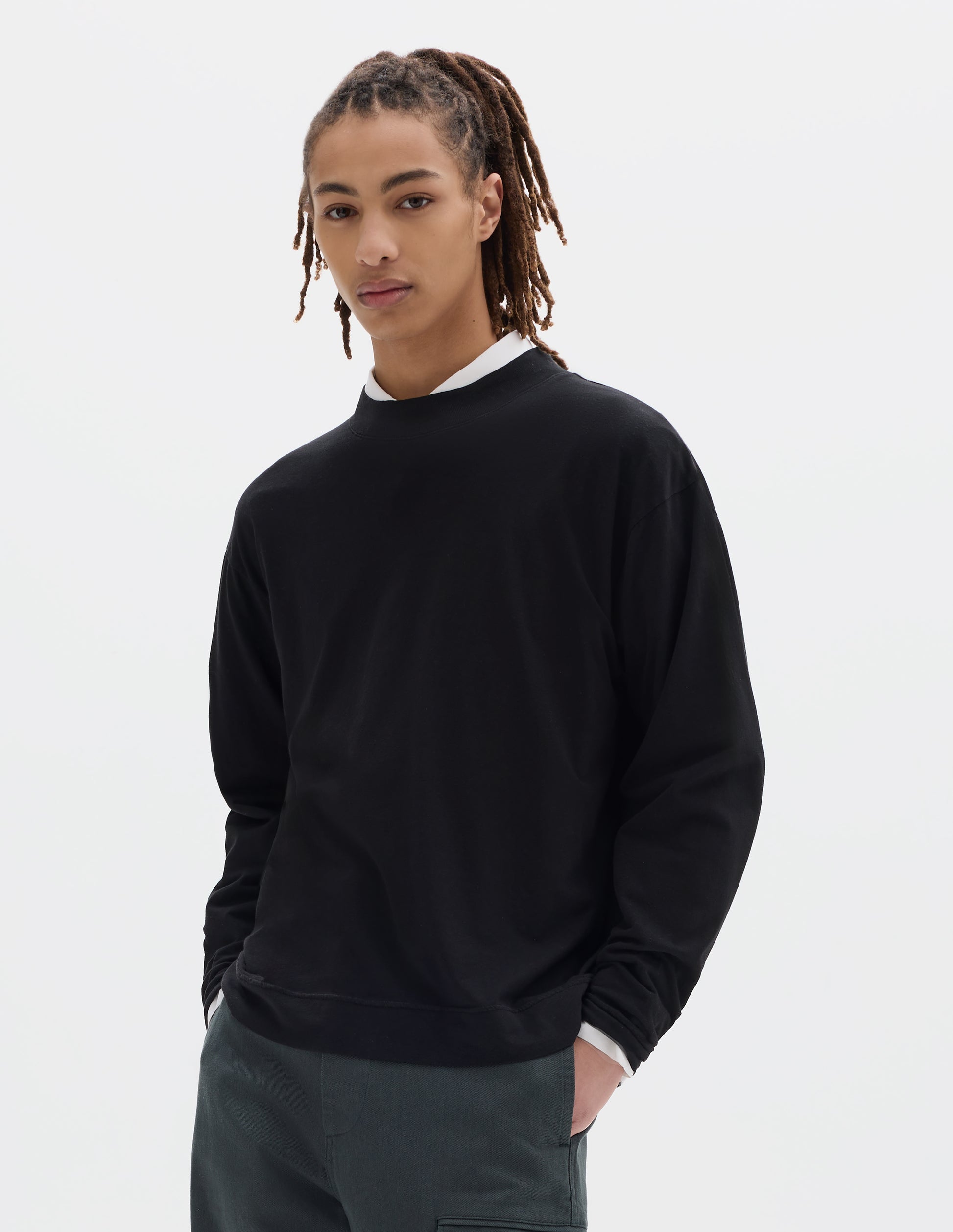 Cropped body image, front view of model wearing a boxy black cotton linen long sleeve crew neck jersey. Worn over a white shirt, styled with dark green-blue cargo trousers.