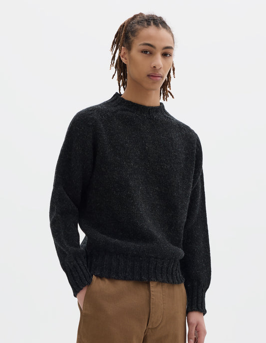 Cropped body image, front view of model wearing dark grey long sleeve wool jumper, with contrast ribbing on neckline, cuffs and hem. Styled with brown trousers.