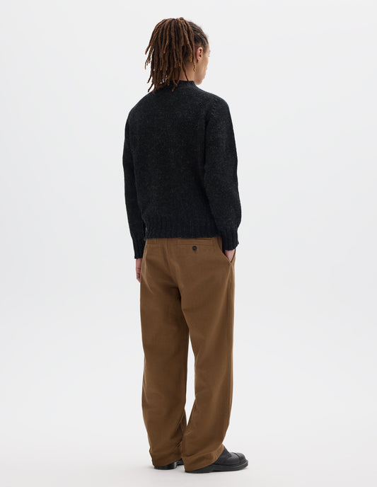Full body image, back view of model wearing dark grey long sleeve wool jumper, with contrast ribbing on neckline, cuffs and hem. Styled with brown trousers and black leather shoes.
