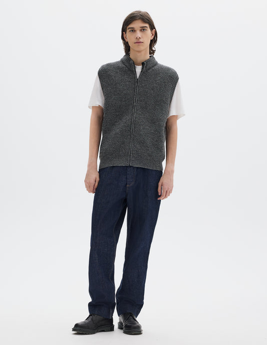 Full body image, front view of model wearing grey knitted wool sleeveless gilet, with rib neck, armholes and hem, and a Vislon zip. Styled over white t shirt, with blue denim jeans and black leather shoes.