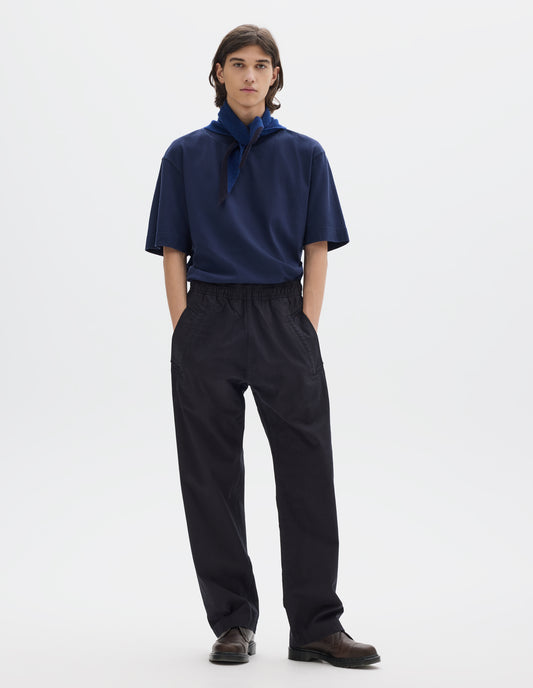 Full body image, front view of model wearing relaxed dark blue joggers with elasticated waist and deep welt pockets. Styled with a relaxed blue short sleeve t-shirt, blue and navy wool scout scarf and dark brown leather shoes.