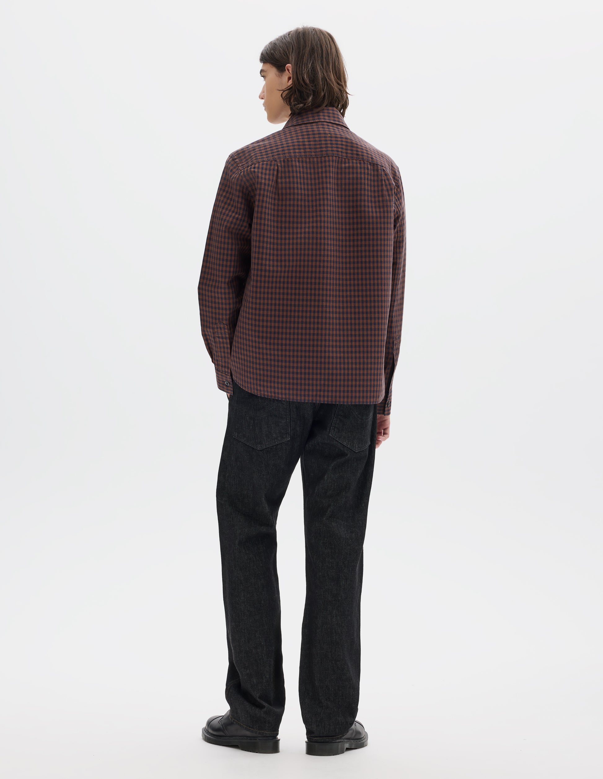 Full body image, back view of model wearing brown and dark blue check cotton linen shirt, with back yoke and button cuffs. Styled with white t shirt, black jeans and black shoes.