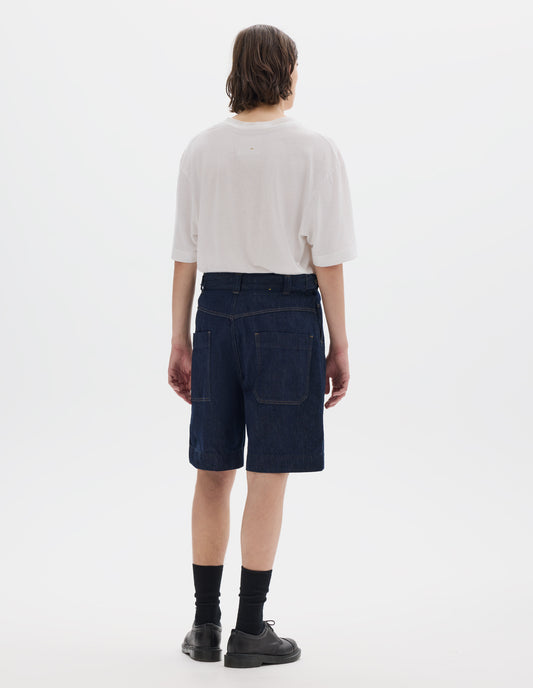 Full body image, back view of model wearing dark blue relaxed denim twill shorts with metal button tab waist adjusters, belt loops and patch pockets. Styled with white short sleeve T shirt, black socks and black leather shoes.