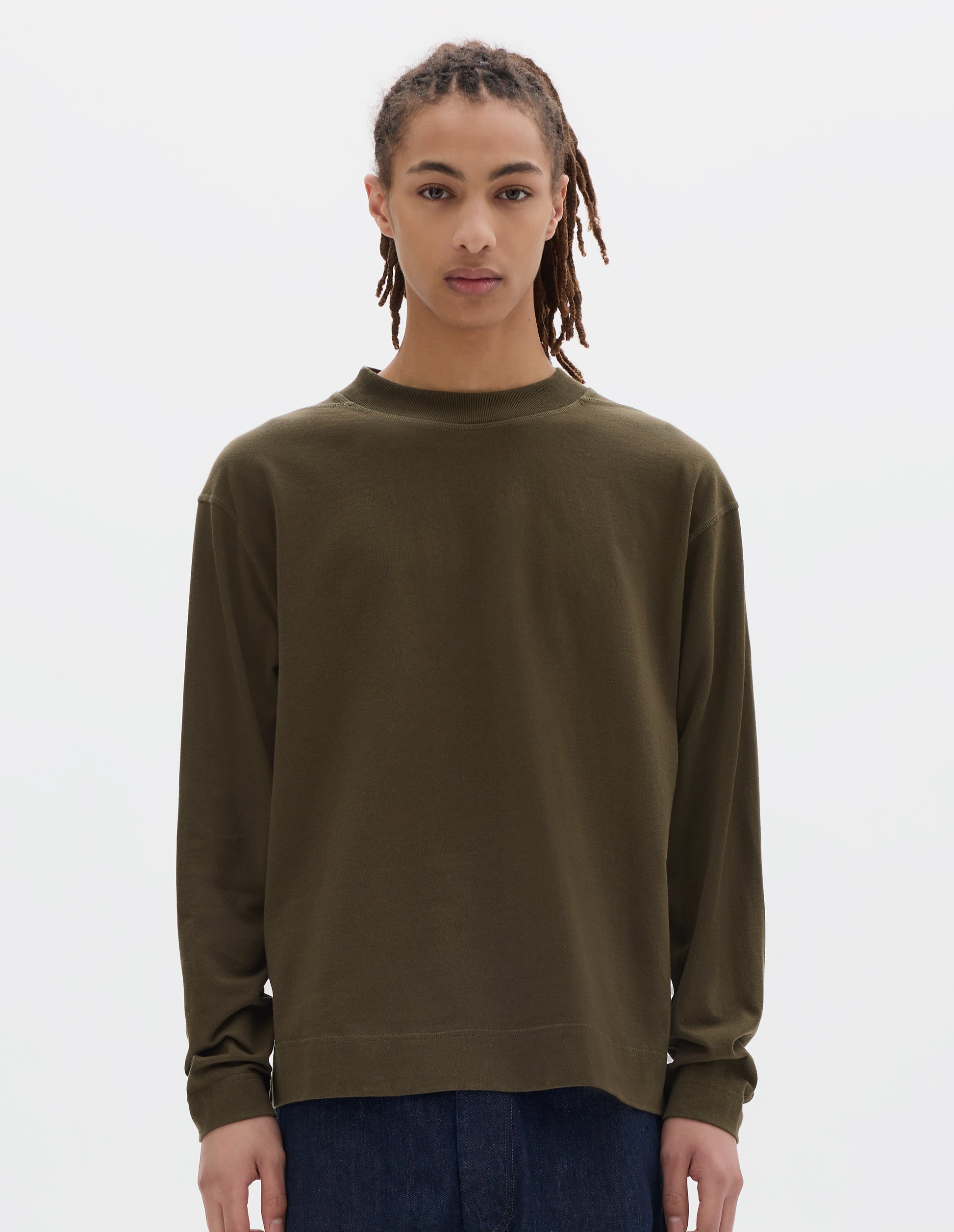 Cropped body image, front view of model wearing a brownish green cotton t shirt, with long sleeves, a deep ribbed collar and ribbed triangle insert on the shoulder. Styled with dark blue relaxed denim twill shorts.