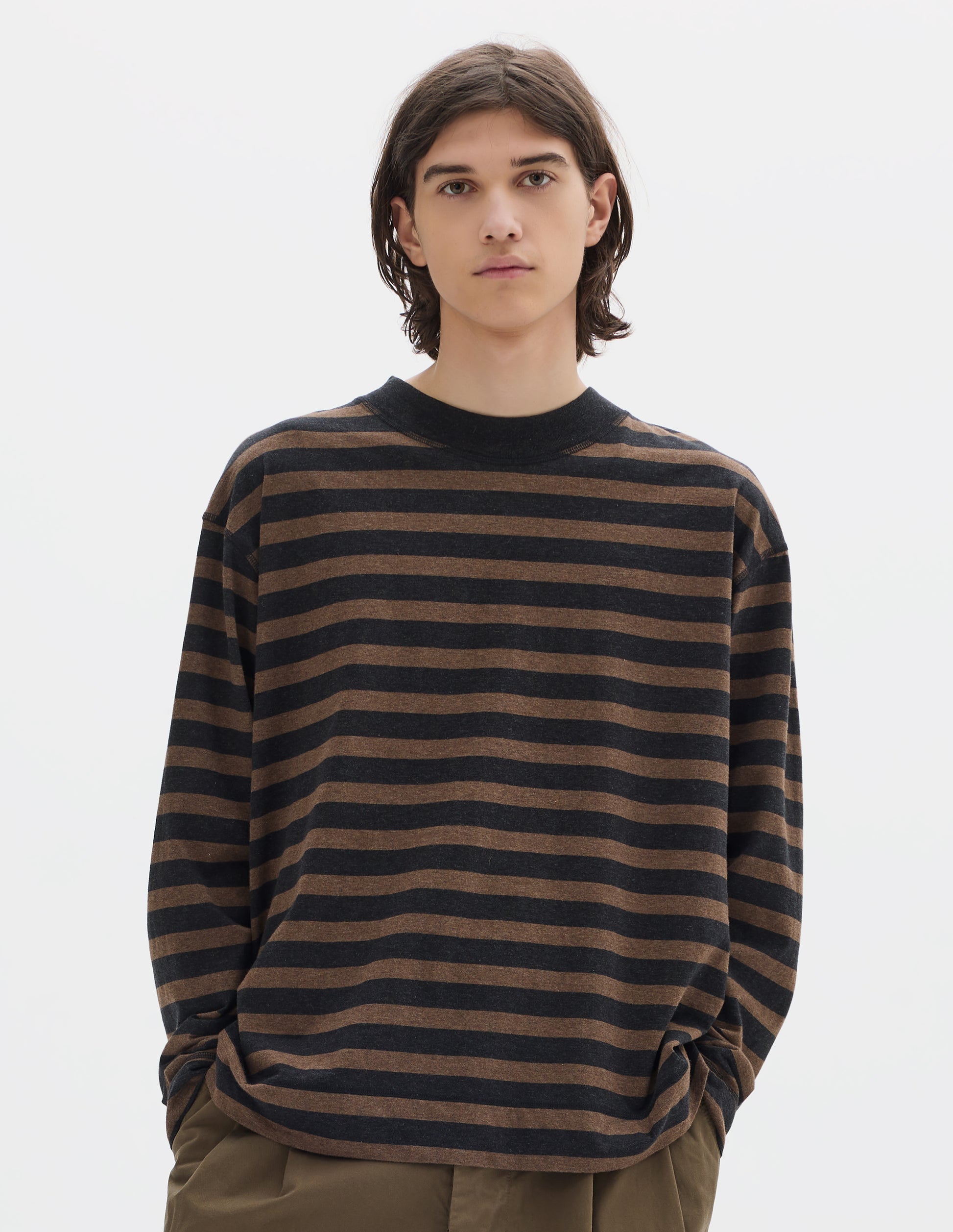 Cropped body image, front view of model wearing black and brown stripe crew neck long sleeve jersey, rib trim on cuff and neck, flatlock stitch seam detailing. Styled with khaki trousers.