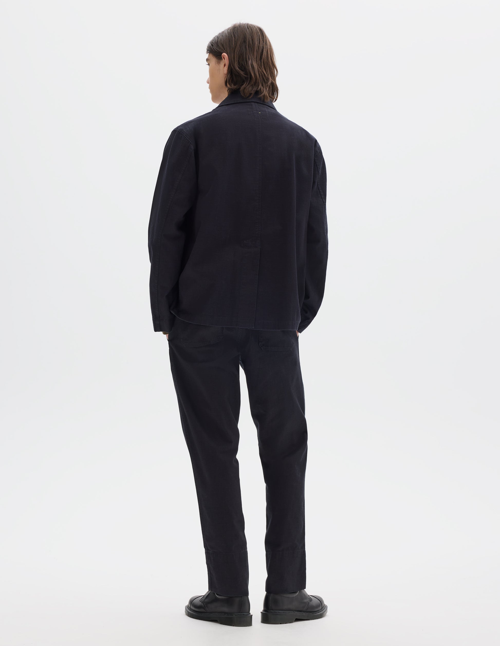 Full body image, back view of model wearing indigo blue twill blazer with back centre vent. Styled with matching indigo blue twill trousers and black leather shoes.