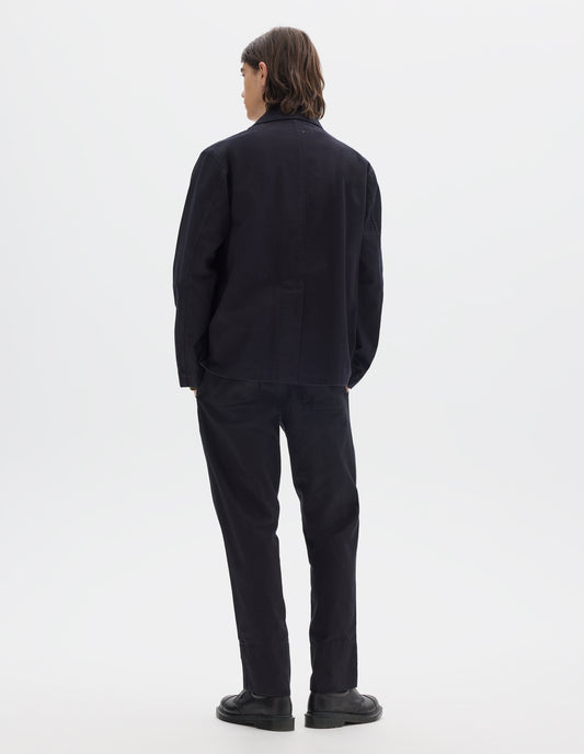 Full body image, back view of model wearing indigo blue twill blazer with back centre vent. Styled with matching indigo blue twill trousers and black leather shoes.