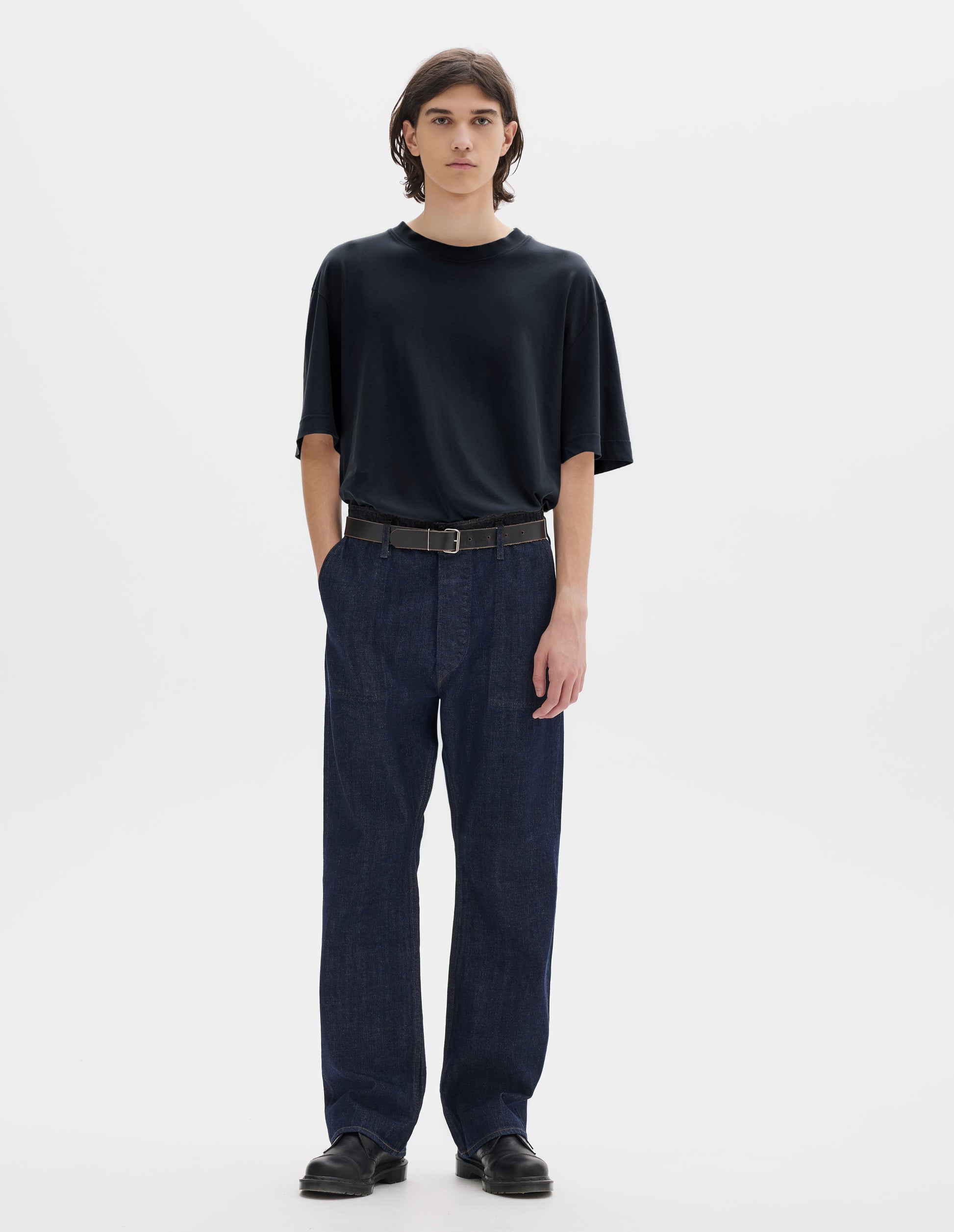 Full body image, front view of model wearing navy blue short sleeve cotton linen t-shirt with contrast rib on neck, worn tucked in to blue denim trousers with black leather belt and black leather shoes.