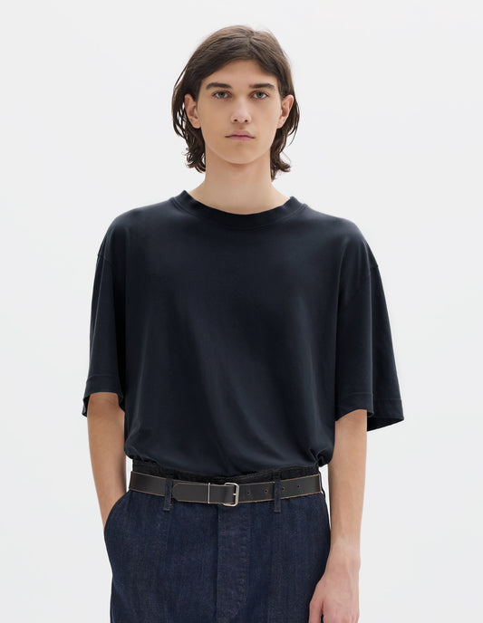 Cropped body image, front view of model wearing navy blue short sleeve cotton linen t-shirt with contrast rib on neck, worn tucked in to blue denim trousers and black leather belt.