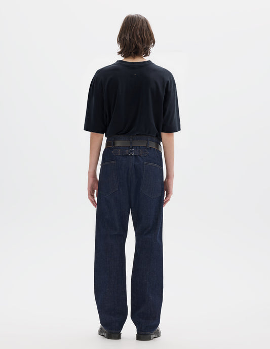 Full body image, back view of model wearing navy blue short sleeve cotton linen t-shirt with contrast rib on neck, worn tucked in to blue denim trousers with black leather belt and black leather shoes.