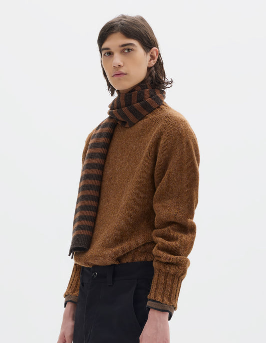 Cropped body image, front view of model wearing a tonal brown stripe wool scarf, an orangey brown wool sweater and black flat fronted trousers.