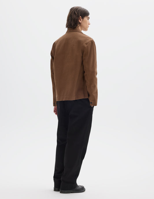 Full body image, back view of model wearing a brown cotton blazer with button-adjustable cuffs. Styled with a black cotton trousers and black leather shoes.