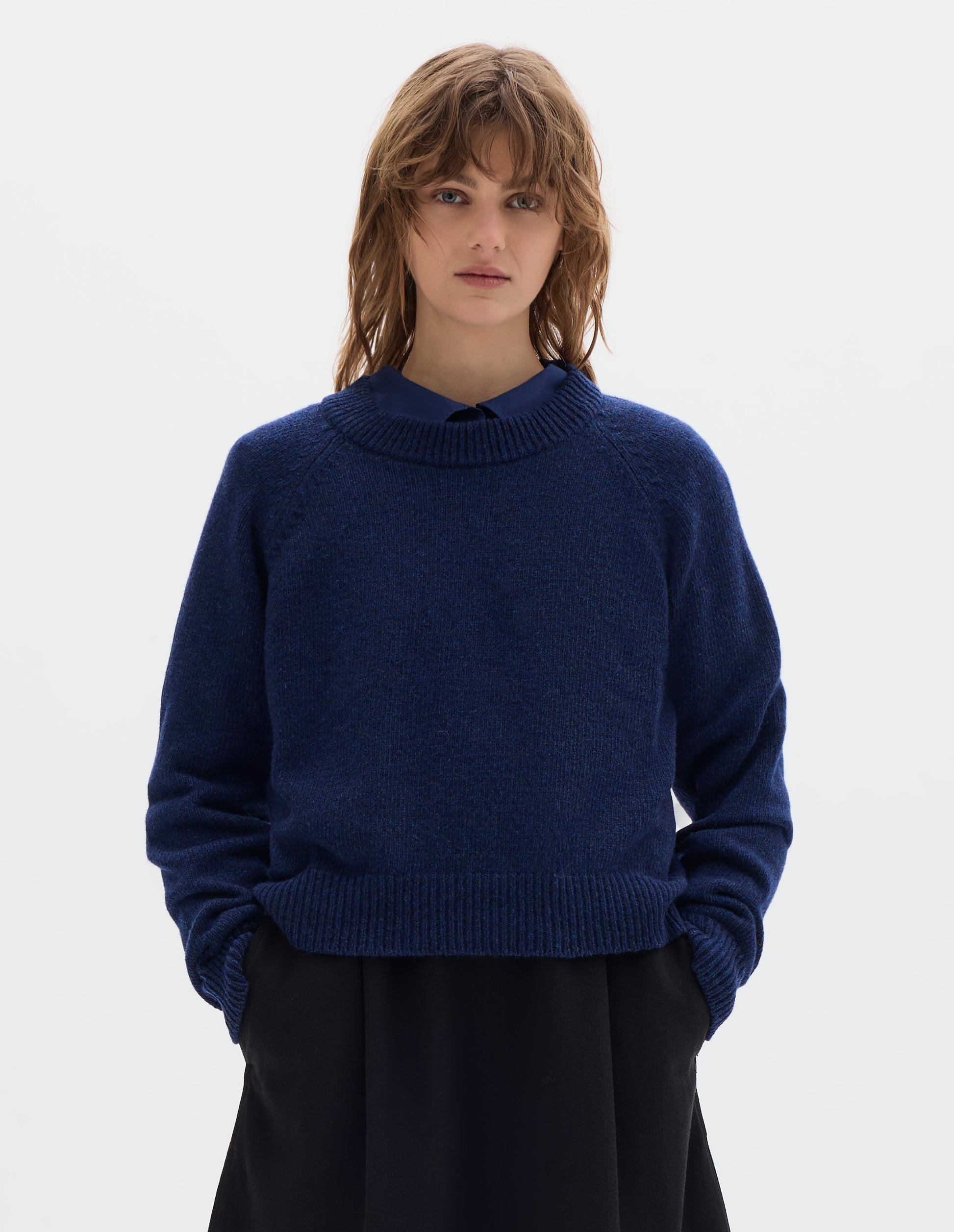 Cropped body image, front view of model wearing blue lambswool jumper, with  crew neck, raglan sleeves, and ribbed neck, cuffs and hem, front flat lay view. Styled with blue shirt and black skirt.
