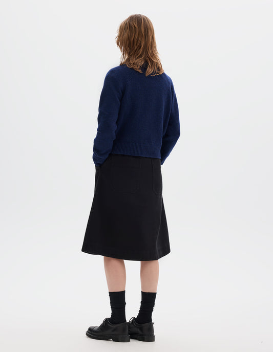 Full body image, back view of model wearing blue lambswool jumper, with crew neck, raglan sleeves, and ribbed neck, cuffs and hem. Styled with black skirt, black socks and shoes.