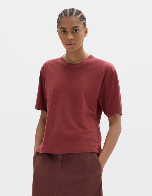 Cropped body image, front view of model wearing a boxy red short sleeve linen cotton t shirt with vent split hem. Styled with a red-brown cotton skirt.