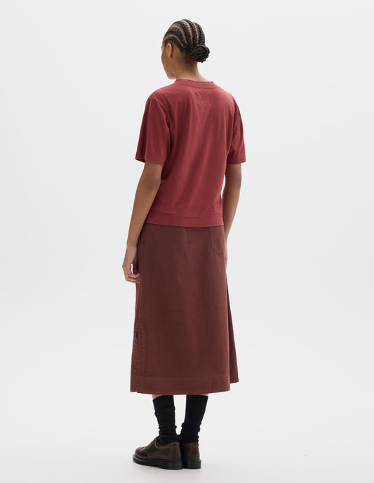 Full body image, back view of model wearing a boxy red short sleeve linen cotton t shirt. Styled with a midi red-brown cotton skirt with a back patch pocket, black socks and brown leather shoes.