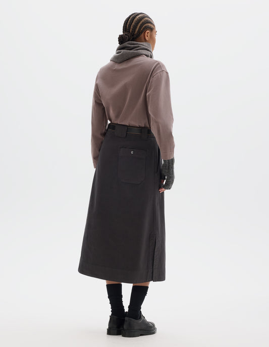 Full body image, back view of model wearing dark brown A line skirt with side splits, belt loop detail on back and back patch pocket with reinforced stitch detailing. Styled with lilac long sleeve top tucked in, black leather belt, grey scarf and matching fingerless gloves. With black socks and black leather shoes.