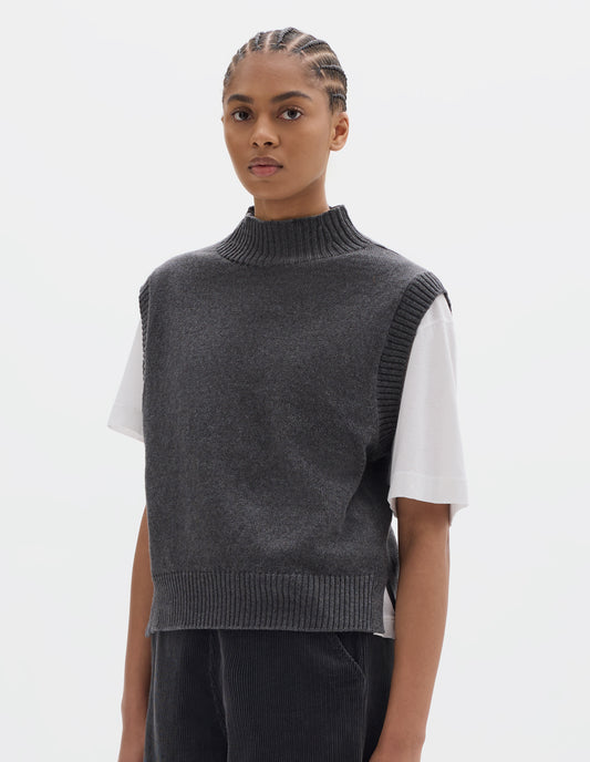 Cropped body image, front view of model wearing a grey wool cotton slipover with a high rib neck, rib armholes and hem and split stepped hem. Styled over a white t shirt and dark grey corduroy trousers.