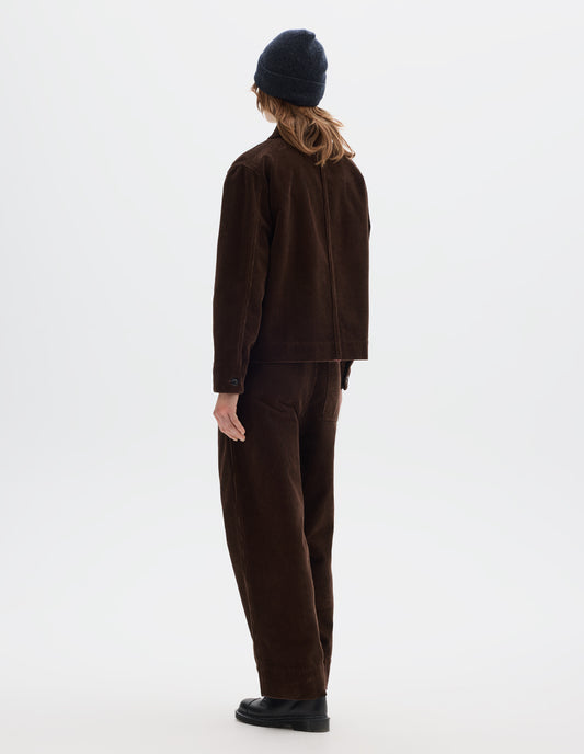 Full body image, back view of model wearing a brown corduroy jacket with shirt cuffs. Styled with matching cord trousers, dark grey beanie and black leather shoes.