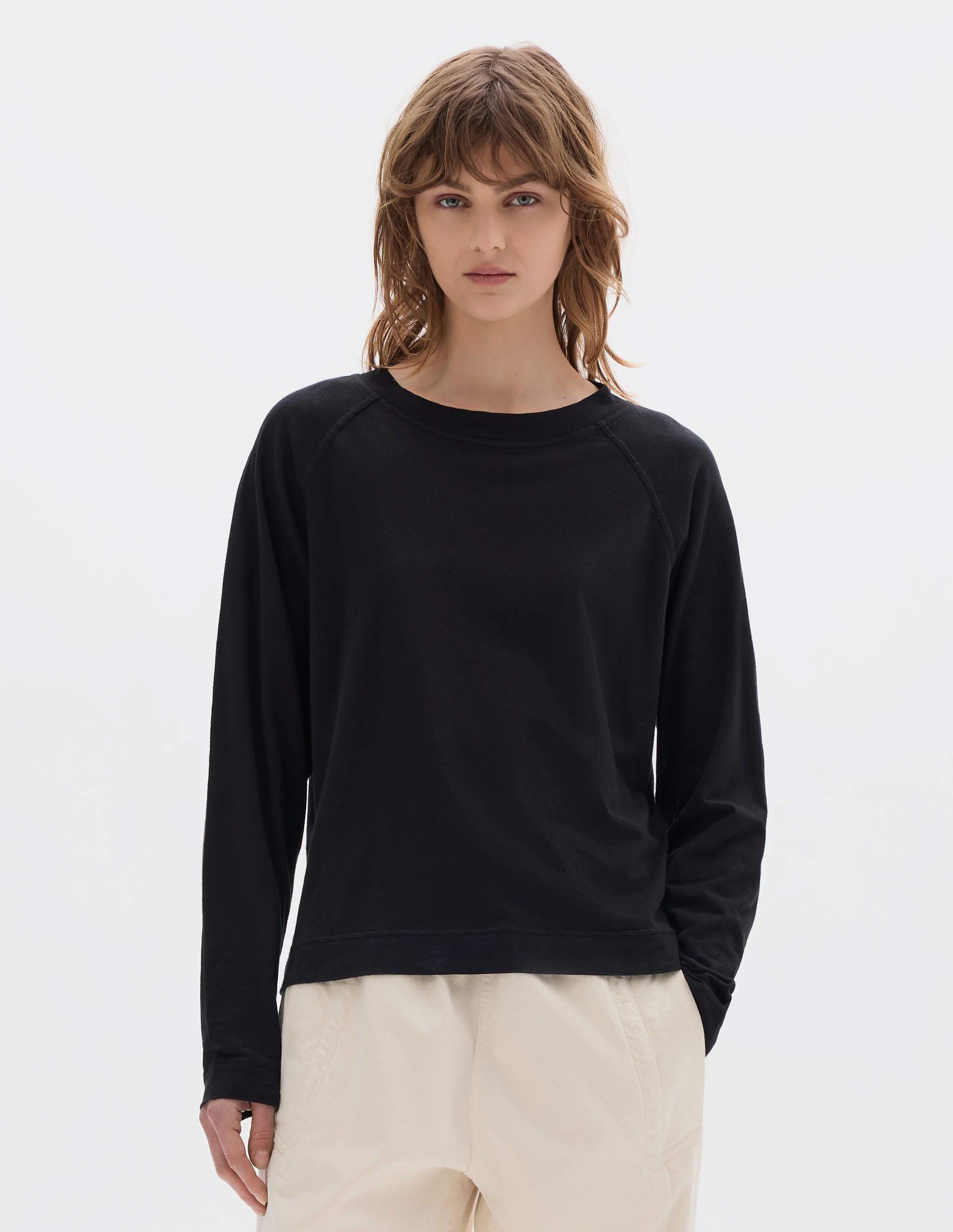 Cropped body image, front view of model wearing a black cotton linen raglan t shirt with a rib crew neck. Styled with jogger style off white trousers.