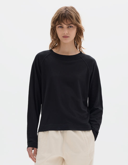 Cropped body image, front view of model wearing a black cotton linen raglan t shirt with a rib crew neck. Styled with jogger style off white trousers.