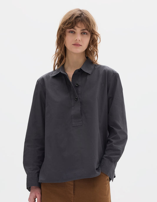 Cropped body image, front view of model wearing a dark grey shirt with an A line cut, constructed with a raised half placket. Styled with brown tan trousers.