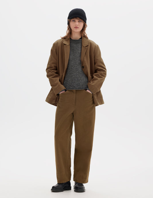 Full body image, front view of model wearing a brown cotton blazer, worn open over a grey wool jumper. Styled with a black wool beanie, matching brown flat front straight leg cotton trousers and black leather shoes.