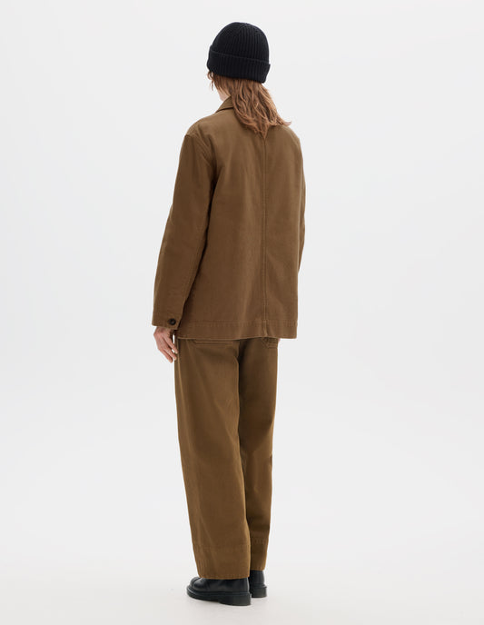 Full body image, back view of model wearing a a brown cotton blazer which features grown-on cuffs with a wide placket opening, centre back seam detailing. Styled with a black wool beanie, matching brown straight leg cotton trousers and black leather shoes.