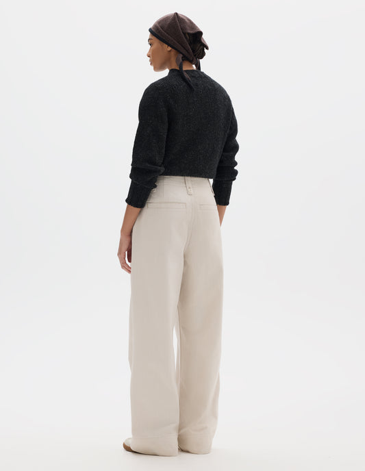 Full body image, back view of model wearing off white trousers with grown-on waistband, button-fastening belt loops, and two back welt pockets. Styled with dark grey jumper tucked in, brown knitted scarf worn on head and white trainers with gum sole.